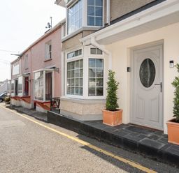 Exterior view of a row of houses along a street with potted plants by a front door at Bodwena in Moelfre