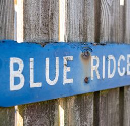 A blue wooden sign with the words blue ridge attached to a wooden fence at Blue Ridge in Polzeath