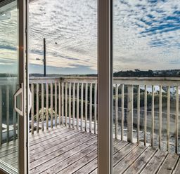 A wooden balcony with railing seen through glass sliding doors at Blue Ridge in Polzeath