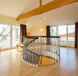 An open living area with a spiral staircase wooden chairs glass doors and brown curtains at Blue Ridge Polzeath