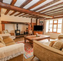 A living room with exposed wooden beams a wood burning stove sofas a wooden coffee table and a television at Manor Farm House in Bacton