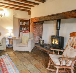 A living room with a fireplace an armchair a rocking chair a sofa a wooden coffee table and a bookshelf at Manor Farm House in Bacton