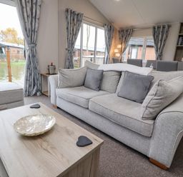 A living room with a grey sofa and cushions a wooden coffee table and shelves at Fountain View in Warton near Carnforth