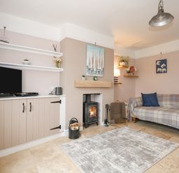 A living room with a plaid sofa a wood burner and a television on a cabinet at Beck View in Sheringham