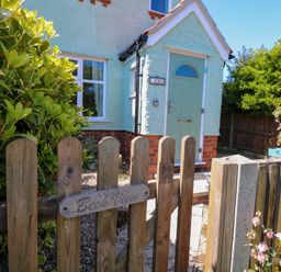 A wooden gate with a Beck View sign leading to a small house with a light blue door and green plants in Sheringham