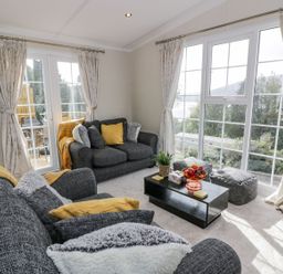 A living room with two grey sofas yellow cushions a black coffee table with a fruit bowl and a plant and large windows with curtains at 11 Mansion View in Helensburgh near Kilcreggan