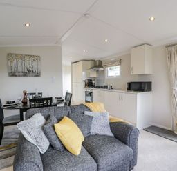 An open plan living room with a grey sofa and yellow cushion a dining table with chairs and a kitchen with white cabinets and appliances at 11 Mansion View in Helensburgh near Kilcreggan