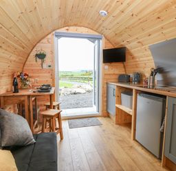 A wooden pod interior with a small kitchen area and dining table with stools at Parys Pod in Amlwch