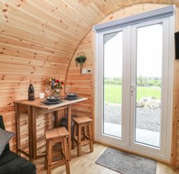 A small dining table with two stools near glass doors in a wooden cabin at Parys Pod in Amlwch