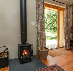 A living room with a wood stove and door leading outside at Brambly Cabin in Crediton
