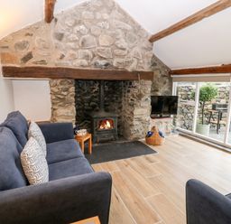 A living room with a stone fireplace a wood burning stove blue sofas and large windows at Y Bwthyn in Dyffryn Ardudwy