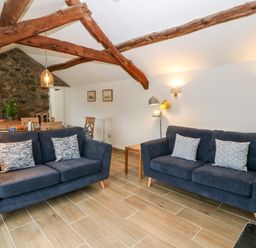 A living room with two blue sofas and wooden beams at Y Bwthyn in Dyffryn Ardudwy