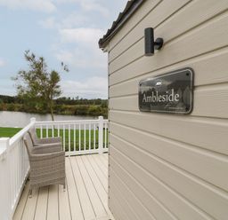 A balcony with two wicker chairs overlooking a lake and trees at 10 Cheviot View in Haggerston near Lowick