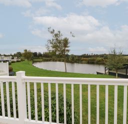 A view of a pond with grass and trees from a white balcony railing at 10 Cheviot View in Haggerston near Lowick