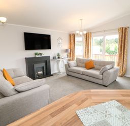 A living room with two grey sofas, a wall-mounted TV, a black fireplace, plants, and yellow patterned curtains at Mildred's Lodge in Felton