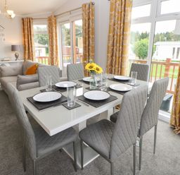 A dining table with six chairs set with plates and glasses in a room with yellow patterned curtains and a gray sofa at Mildred's Lodge in Felton