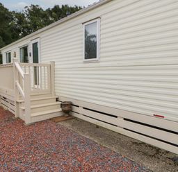An exterior view of a beige mobile home with steps leading to a small porch and a gravel ground at Hedgehog Retreat in Felton