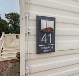 A close up of a sign with number 41 and Hedgehog Retreat on the side of a beige building with steps and railing leading to a door outside at Hedgehog Retreat in Felton
