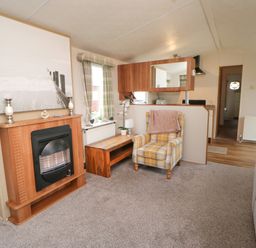 A living room with a fireplace a yellow plaid armchair a wooden bench and a kitchen area at Hedgehog Retreat in Felton