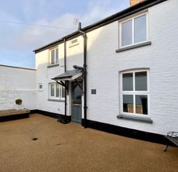 An exterior courtyard with a white brick house entrance bench and a small planter at Secret Cottage Southwold