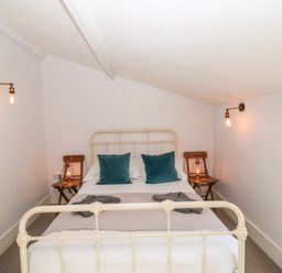 A bedroom with a metal framed bed two teal pillows wooden side tables lamps on tables and wall lights at Secret Cottage Southwold