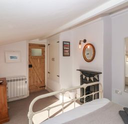 A bedroom with a white metal bed frame wooden door wooden dresser and wall mirror at Secret Cottage Southwold