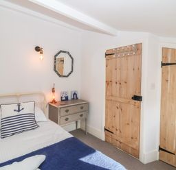 A bedroom with a metal bed frame a side table with a lamp and a mirror wooden doors at Secret Cottage Southwold