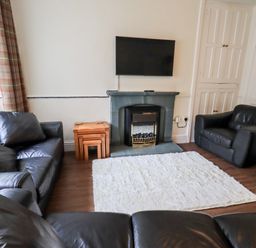 A living room with black leather sofas a wall-mounted TV a fireplace white rug and wooden nesting tables at 6 Calgarth View in Windermere