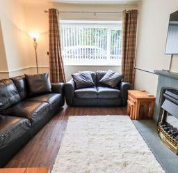 A living room with black leather sofas a white rug wooden nesting tables a floor lamp and a fireplace at 6 Calgarth View in Windermere