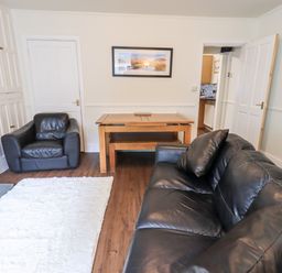 A living room with black leather sofas a wooden dining table and bench a white rug and a fireplace at 6 Calgarth View in Windermere