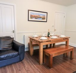 A dining area with a wooden table set with plates glasses and a bottle next to a black armchair at 6 Calgarth View in Windermere