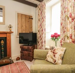 A living room corner with green armchair, floral cushion, TV on stacked storage boxes, wooden fireplace, and floral curtains at 12 Castlegate in Pickering