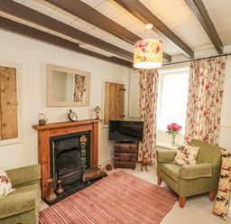 A sitting room with two armchairs a fireplace a television and floral curtains at 12 Castlegate in Pickering