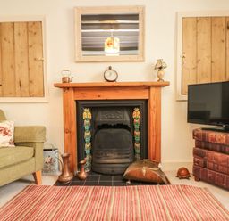 A living room with a fireplace two wooden shuttered windows a green armchair a television on a book stack and a striped rug at 12 Castlegate in Pickering