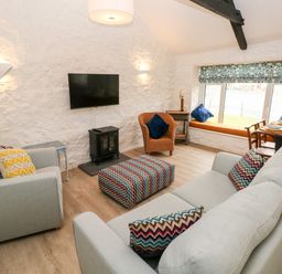 A living room with two light sofas a patterned ottoman a wicker chair and a window seat at Bluebell Cottage Jameston near Manorbier