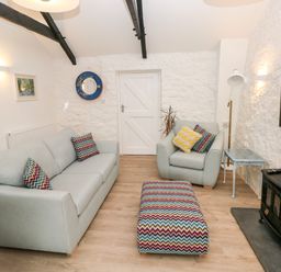 A living room with a sofa armchair ottoman television and stove at Bluebell Cottage Jameston near Manorbier