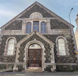 Stone facade of English Presbyterian Church with arched windows and double doors at The Church in Holyhead