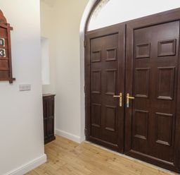A hallway with dark wooden double doors and a wooden hymn board on a white wall at The Church in Holyhead