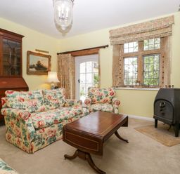 A sitting room with floral upholstered sofa and chairs wooden coffee table wood stove and cabinet at Ham cottage East Lambrook near South Petherton