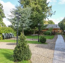A garden with gravel paths lamp posts bushes stacked chairs and a wooden shed at Pheasant in Bedale