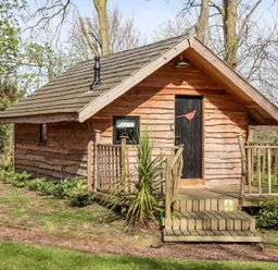 A wooden cabin with a small porch and steps in a garden surrounded by trees and plants at Pheasant in Bedale