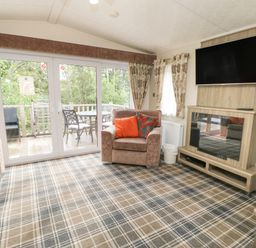 A living room with armchairs a wall mounted tv and glass doors leading to a deck with outdoor furniture at Bock Retreat in Felton