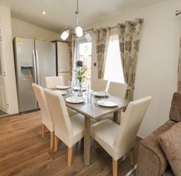 A dining area with a table set for six with white chairs near beige curtains and a stainless steel refrigerator at Bock Retreat in Felton