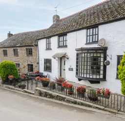 A street view of stone and white cottages with flower pots along a metal fence at Church View Cottage Near Looe