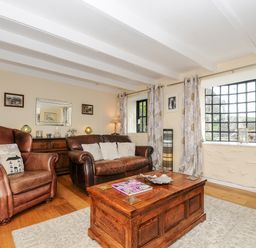 A living room with brown leather armchair and sofa a wooden chest coffee table windows with curtains and wall mirror at Church View Cottage Near Looe