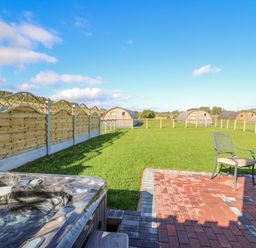 A backyard with a hot tub patio chair grassy field wooden fence and small wooden cabins at Poppy in St Harmon near Rhayader