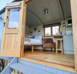 An open door showing a small room with a bed, armchair, window, and kitchenette at Poppy in St Harmon near Rhayader