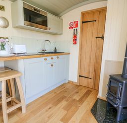 A compact kitchen area with wooden stools a microwave sink wooden cabinets and a black stove at Poppy in St Harmon near Rhayader