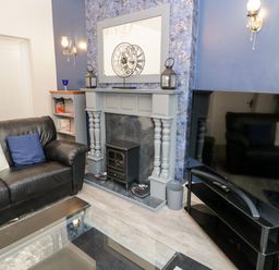 A living room with a black leather sofa a fireplace with a clock on the mantel and a television on a black stand at Gwyder in Penmaenmawr