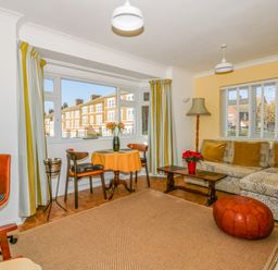 A living room with a patterned sofa and mustard cushions a wooden coffee table and a red pouf at See The Sea in Hunstanton